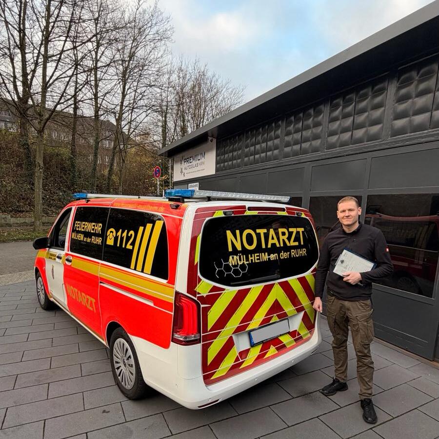 Ein lächelnder Mann mit heller Haut steht neben einem rotgelben Notarztwagen